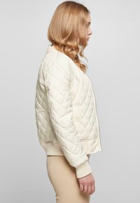 Quilted krem bomberjakke med ribbestrikkede mansjetter og kant, med glidelås og sidelommer. Myk tekstur og litt kortere design.