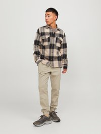 Karirana flanel košulja u bež i mornarskoj plavoj, s dva džepa na prsima i zatvaranjem na dugmad; uparena s bež uskim hlačama i sivim tenisicama.