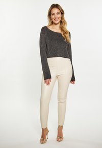 Pulover scurt metalic negru cu mâneci lungi, asortat cu pantaloni din piele artificială bej cu talie înaltă și pantofi cu toc aurii cu bretele.