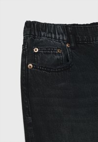 Jeans in denim nero con cintura elastica, dotati di due tasche anteriori, rivetti in rame e un tessuto liscio, leggermente strutturato.