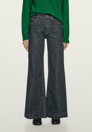 Jeans scuri a gamba larga con vita alta, caratterizzati da cuciture a contrasto e orlo grezzo. Abbinati a un maglione verde per creare contrasto.