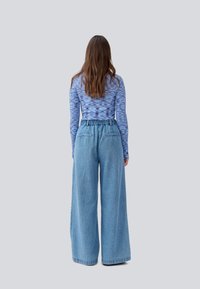Blå mønstrete langermet topp kombinert med høyt liv, vid benlys lyseblå denimbukser. Teksturert overflate, elastisk midje, to baklommer.