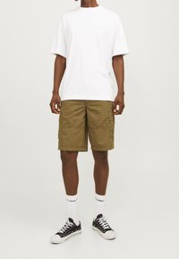 Vit bomull t-shirt, avslappnad passform; olivgröna cargo-shorts med flera fickor; svarta sneakers med vita accenter och strumpor.