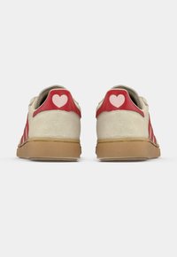 Άσπρα και κόκκινα παπούτσια με φινίρισμα από σουέντ, που διαθέτουν κόκκινη δερμάτινη γλώσσα στο τακούνι στολισμένη με ροζ καρδιά, και σόλα από καουτσούκ.