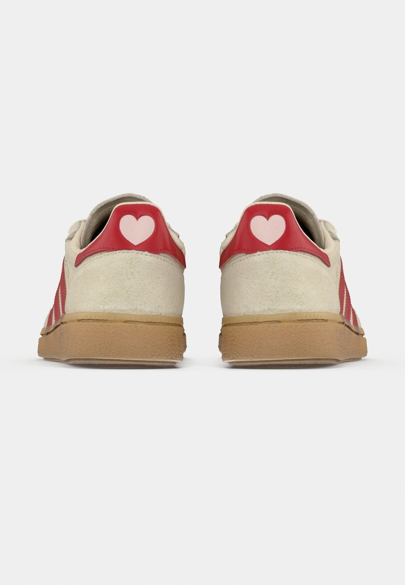 White and red sneakers with a suede finish, featuring a red leather heel tab adorned with a pink heart, and a gum sole.