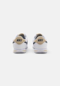 Valged Nike'i spordijalatsid beeži ja tumesinise aktsendiga, millel on tekstureeritud ülemine osa, kumer konts ja logo taga.