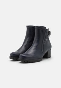 Botas de tobillo de cuero azul marino con punta ligeramente redondeada, acento de hebilla lateral y suela de goma texturizada. Presenta un tacón moderado para mayor soporte.