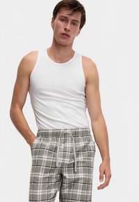 Biały top na ramiączkach w połączeniu z szarymi szortami w kratę, posiadającymi pasek ze ściągaczem i kontrastujące białe linie w wzorze.