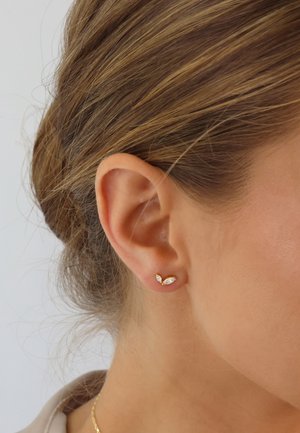 Gold stud earrings featuring clear marquise-cut stones, set in a leaf-like design. The earrings are worn on a light skin tone.