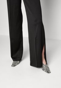 Zapatos de tacón puntiagudos con estampado de cebra combinados con pantalones de pierna ancha negros con aberturas laterales para una silueta fluida y un diseño elegante.