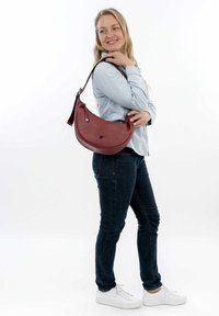 Red leather crossbody handbag with a curved shape, featuring a zipper and a silver accent. Worn over the shoulder.