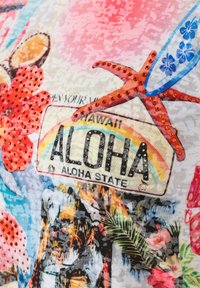 Bunt bedruckter Stoff mit tropischen Motiven, einschließlich eines Nummernschildes mit der Aufschrift "ALOHA", Blumen, Seesternen und einem Surfbrett. Glitzernde Akzente sind sichtbar.