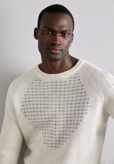 Cremefarbener Strickpullover mit einem strukturierten grauen Muster, Rundhalsausschnitt und gerippten Bündchen. Weicher, dicker Stoff mit lockerer Passform.