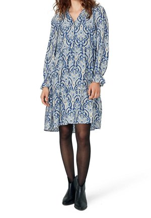 Mujer con vestido azul y blanco de manga larga hasta la rodilla, medias negras y botines negros.