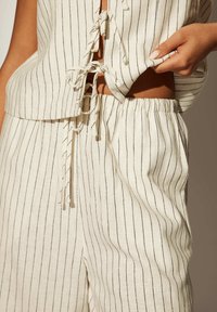 Conjunto de dos piezas de rayas blancas y negras que incluye una blusa sin mangas con detalle de lazo y pantalones con cintura elástica. Tela texturizada, corte relajado.
