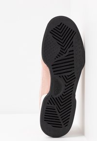 Semelle en caoutchouc noir d'une chaussure rose avec des motifs géométriques en relief, présentée sur un fond blanc.