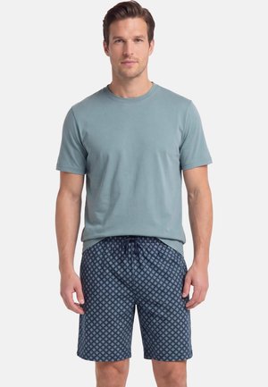Man draagt een effen lichtblauw T-shirt met korte mouwen en marineblauwe korte broek met patroon en een taillekoord, staand tegen een witte achtergrond.