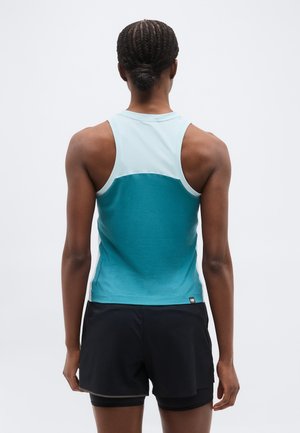 Žena s kosom upletenom u punđu, nosi sportski gornji dio bez rukava u tirkiznoj i svijetloplavoj boji te crne kratke hlače, stoji okrenuta leđima.