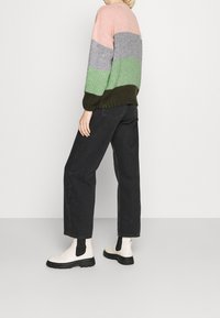 Maglione lavorato a maglia nei toni del rosa, grigio, verde e verde scuro, abbinato a jeans neri a gamba larga e stivaletti color crema con dettagli neri.