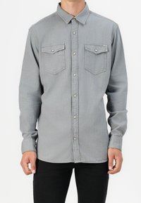 Camicia a maniche lunghe grigia chiara con chiusura a bottoni, due tasche sul petto e una texture morbida. Presenta un colletto classico e polsini con bottoni.