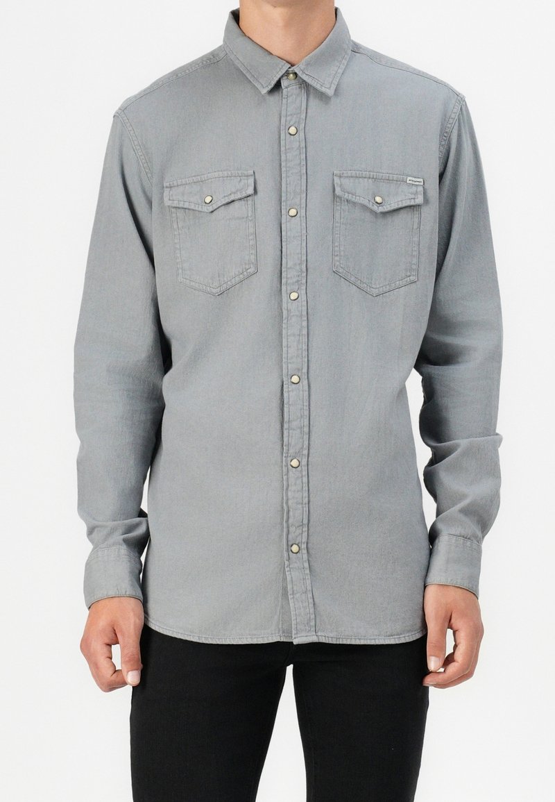 Camicia a maniche lunghe grigia chiara con chiusura a bottoni, due tasche sul petto e una texture morbida. Presenta un colletto classico e polsini con bottoni.