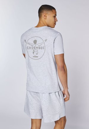 Man wearing light gray T-shirt with graphic of a diver and "Chiemsee" text on back, paired with matching gray shorts.