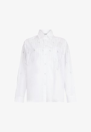 Valge puuvillane nööbitav särk, millel on lõdvestunud lõige, pikad varrukad ja esiküljel dekoratiivsed augumustrid.