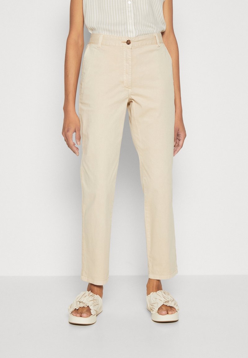 Beżowe lekkie spodnie o prostym kroju, zapinane na guzik, z kieszeniami bocznymi. Noszone z kremowymi, falbanianymi sandałami na płaskiej podeszwie.