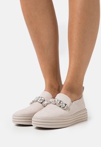 Helle beige Slipper aus Wildleder mit einer dicken Plattform und einer dekorativen metallischen Kettenakzentierung an der Vorderseite.