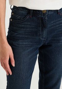 Vaqueros de mezclilla azul oscuro con una cintura de altura media, diseño de cinco bolsillos, detalles en dorado y costuras sutiles en la parte delantera y en los bolsillos.