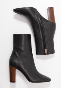 Black leather ankle boots with a pointed toe, side zip closure, and a chunky wooden heel. Smooth texture and minimalistic design.