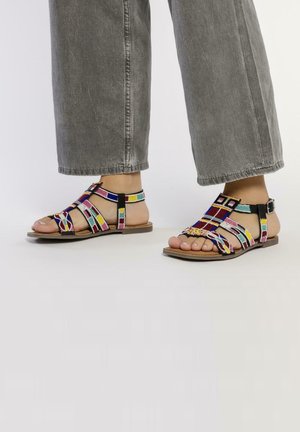 Sandalias tejidas coloridas con una suela plana marrón, que presentan tiras multicolores y un acento de hebilla negra.