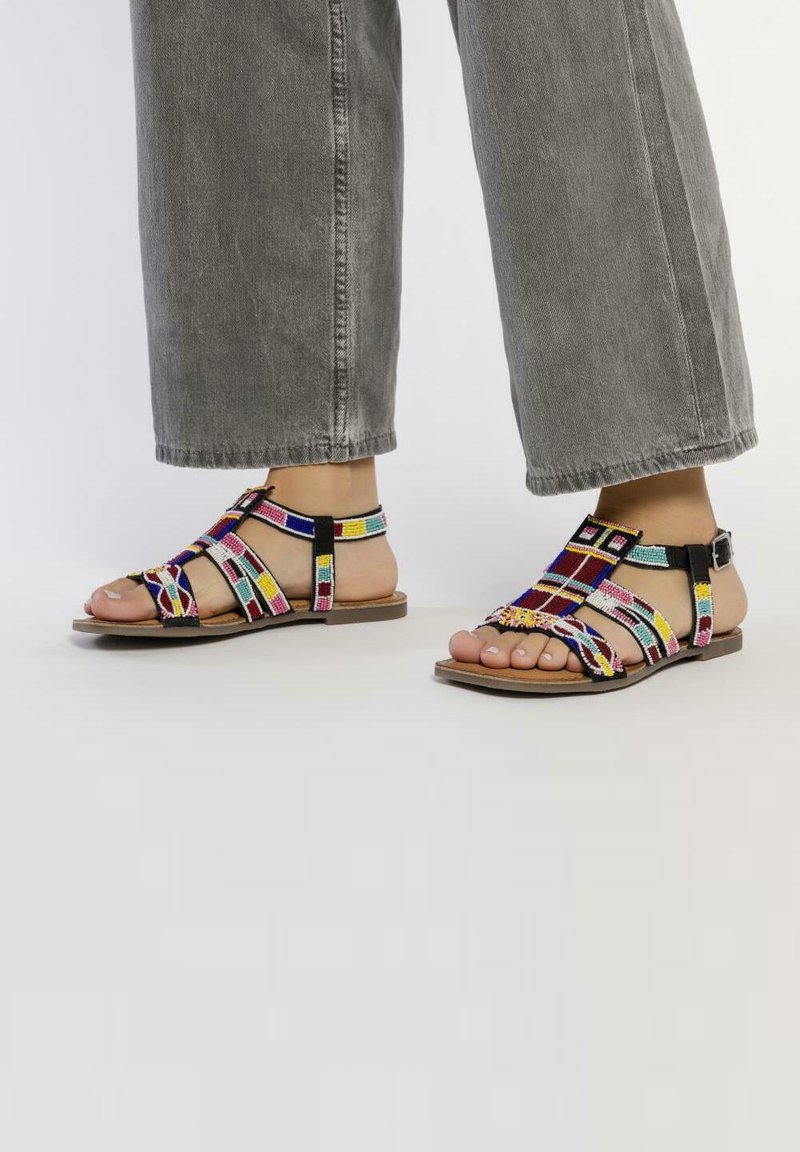 Sandalias tejidas coloridas con una suela plana marrón, que presentan tiras multicolores y un acento de hebilla negra.