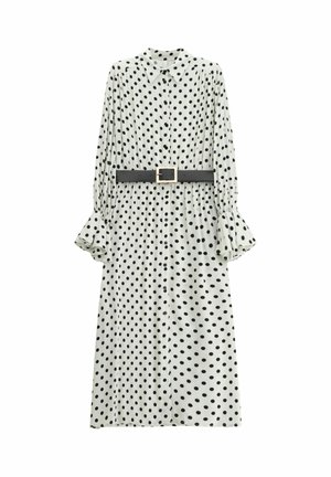 Abito a pois bianco con pois neri, maniche lunghe, chiusura frontale con bottoni e dettagli arricciati. Include una cintura nera con fibbia quadrata.