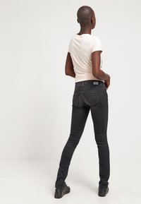 Jeans ajustados negros con una textura suave y detalles de costura sutiles, combinados con una camiseta de color claro ajustada. Diseño de un único bolsillo trasero.