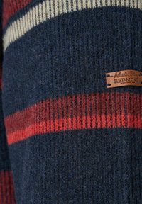 Geweven sweater met een donker marineblauwe basis, grote rode strepen en een crème accent. Inclusief een bruine leren label met merknaam.