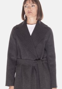 Cappotto di lana grigio con colletto a scialle, vita con cintura e maniche lunghe. Il tessuto ha una texture liscia e dettagli di cucitura sottili.