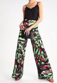 Spodnie o szerokich nogawkach w zielone, brązowe i czerwone wzory. Czarna satynowa koszulka na ramiączkach z koronkową lamówką. Modelka trzyma czarną kopertówkę.