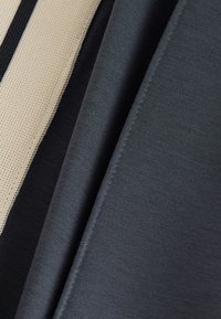 Kolme kangasnäytettä: beige verkkokangas, musta sileä kangas ja tummanharmaa neulos, jotka esittelevät erilaisia koostumuksia ja värejä.