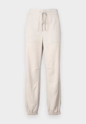 Pantaloni beige leggeri con elastico in vita, dettaglio con coulisse e polsini elasticizzati. Presentano due tasche frontali e una texture liscia.