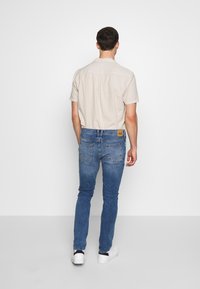 Ljus beige kortärmad skjorta i kombination med blå denimjeans med bakfickor, instoppad i midjan, bärs med vita skor.