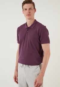 Tumma violetti polo-paita klassisella kauluksella, kolmella napilla ja lyhyillä hihoilla. Yhdistetty vaaleanharmaisiin nauhakuuluspantsuihin.