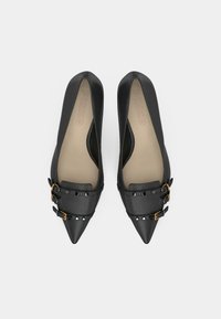 Sapatilhas pretas de bico fino com acabamento suave. Apresentam fivelas em tom dourado e detalhes com tachas nas correias. Solas interiores bege acolchoadas.