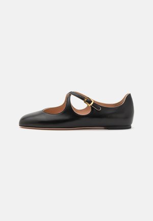 Chaussure plate en cuir noir avec un bout arrondi et un design découpé sur les côtés. Dotée d'une seule sangle avec boucle. Texture lisse, style minimaliste.