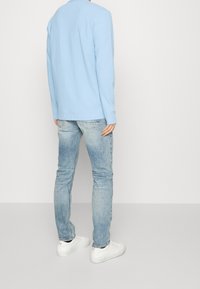 Ljusblå långärmad skjorta, avslappnad passform, matchad med ljus tvättade jeans. Vita sneakers med subtila accenter fulländar den avslappnade stilen.