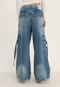 Cargo-byxor i blekt blå denim, med vida ben, flera stora fickor och ett märke med logotyp på midjebandet.