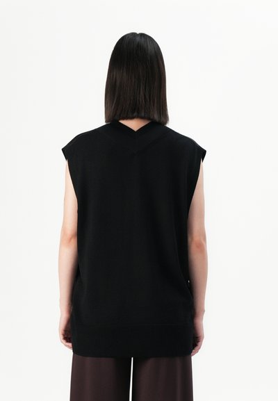 Haut en tricot noir sans manches avec un décolleté en V au dos, offrant une coupe décontractée et une texture subtile. L'ourlet s'étend légèrement sous la taille.