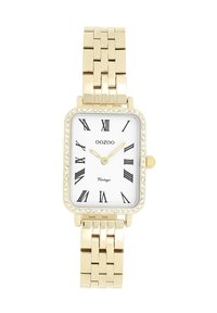 Montre rectangulaire en or avec un cadran blanc, des chiffres romains noirs et une lunette ornée de cristaux. Bracelet en métal à maillons avec finition polie.