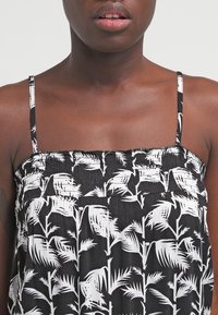 Svart ärmlös topp med en vit botanisk tryck. Rynkad textur vid kroppen med tunna band.