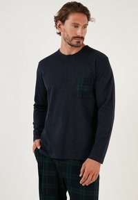 Marineblå langærmet skjorte med en ternet lomme; blødt stof, rund hals, afslappet pasform. Sammen med mørkegrønne ternede pyjamabukser.